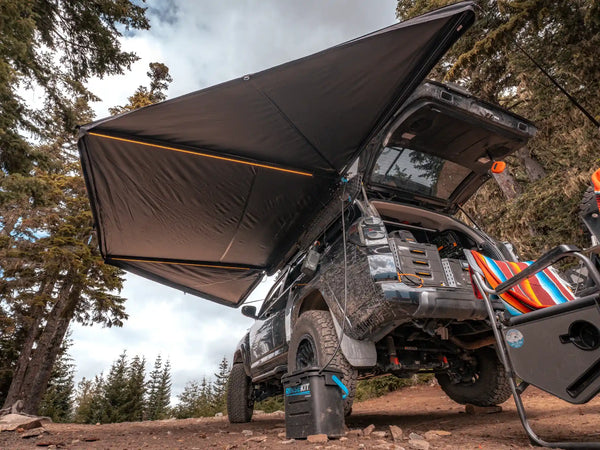 FSR 180 Awning — Lifestyle shot: deployed on a black Toyota 4Runner with LED lights illuminated at a wooded campsite