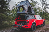 Leitner ACS Forged Bed Rack: fully loaded Ford Raptor on a dry lake bed with a roof top tent, RotoPax fuel cans, and a GearPod storage box all mounted at once
