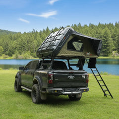Black Ford truck with a rooftop tent set up by a lake on a sunny day.
