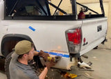Backwoods Adventure Mods Hi-Lite Rear Bumper (2016–2023 Tacoma) — Feature shot: one person installing the bumper at home