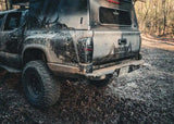 Backwoods Adventure Mods Hi-Lite Rear Bumper (2016–2023 Tacoma) — Lifestyle shot: mud-covered rear bumper on a black Tacoma