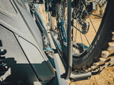 KUAT Piston SR Bike Tray — Lifestyle shot: close-up of a bike's rear wheel and drivetrain locked into the tray with the truck body and dirt trail visible behind it
