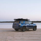 Roofnest Falcon 3 EVO XL Air — Lifestyle shot: closed tent on a blue 4Runner parked on a lakeside beach at dusk. A sleek setup for weekend shoreline trips.