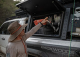 Backwoods Adventure Mods Bed Rack Storage Box (2005–2027 Tacoma) — Lifestyle shot: opening the box to grab fly fishing gear