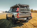 GateKEEPER — Lifestyle shot: fully built overland Super Duty parked in a field, rooftop tent and loaded rack up top, GateKEEPER securing the rear bed.