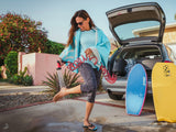 HydroPOD CARRY Portable Shower Kit — Lifestyle shot: scrubbing mud off boots and tools in a garage using the hose, with the tank unit visible on the truck tailgate behind.