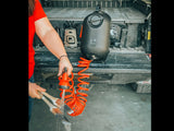 HydroPOD CARRY Portable Shower Kit — Lifestyle shot: scrubbing mud off boots and tools in a garage using the hose, with the tank unit visible on the truck tailgate behind.
