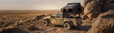 Roofnest Condor Overland 2 Air — Lifestyle shot: open tent on a pickup among red sandstone boulders, a rugged basecamp far from pavement
