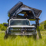 OVS XD Atlas rooftop tent open on a Ford Bronco in a grassy field, ladder down