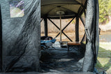 FSR Hub 4 Double — Lifestyle shot: camper inside the tent with a stove running and roll-up walls open to a river view.