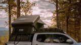 FSR Kali — Lifestyle shot: mounted on an overland bed rack in a forested campsite under a cloudy sky