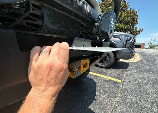Backwoods Adventure Mods Flip-Up License Plate Holder (Hawse Fairlead) — Feature shot: hand lifting the plate to reach the winch line