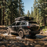 Roofnest Meadowlark 2 XL — Lifestyle shot: closed tent on a Subaru crossing a forest creek. Light enough to go anywhere your wagon does.